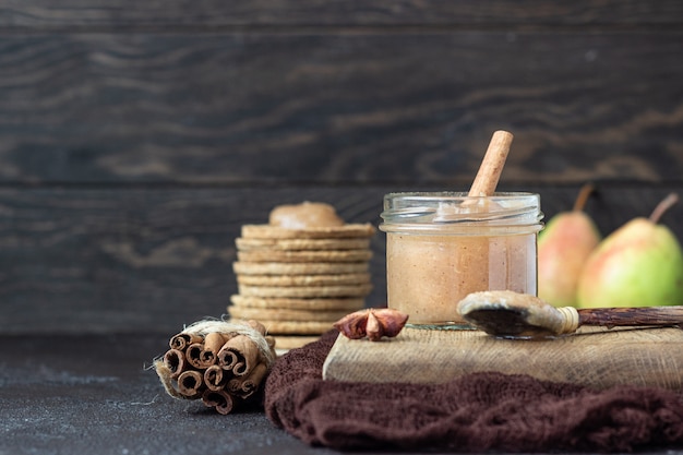 Würzige Birnenmarmelade im Glas, Cracker, Gewürze und Thymian. Brauner Stein.