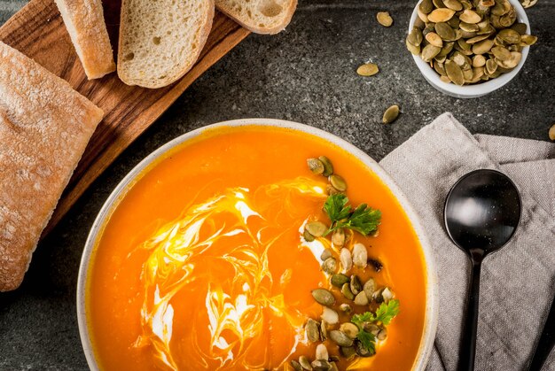 würzige Kürbissuppe mit Kürbiskernen, Sahne und frisch gebackenem Baguette auf schwarzem Steintisch