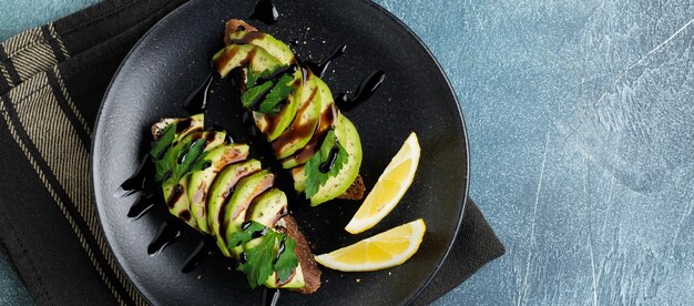 Würzige Roggentoasts mit Avocado, Zitrone und Balsamico-Sauce auf schwarzem Beton altem Hintergrund. Selektiver Fokus. Ansicht von oben