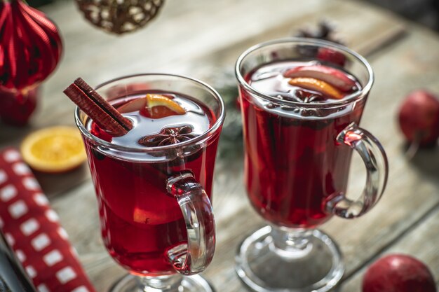 Würziger aromatischer heißer Glühwein in ein paar klaren Gläsern auf einem Holztisch mit festlichen Accessoires. Konzept einer gemütlichen Urlaubsatmosphäre, Neujahrs- und Weihnachtsstimmung