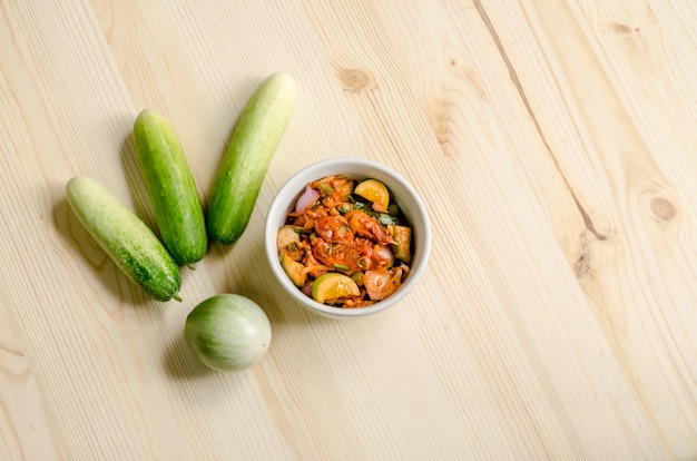 Würziger Salat der in Essig eingelegten Miesmuscheln mit Gurke und thailändischer Aubergine auf Holztisch, thailändisches Lebensmittel.