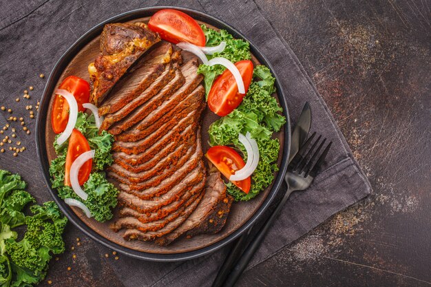 Würziges gebackenes Rindfleisch mit Kohlsalat im Schwarzblech auf dunklem Hintergrund.