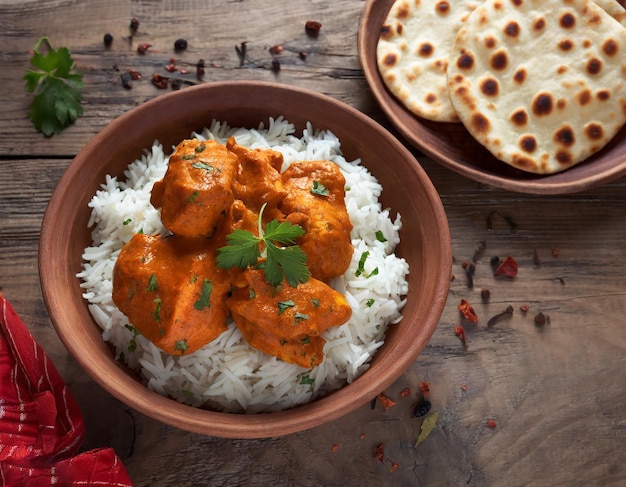 Würziges Hühnchen-Tikka-Masala-Curry, serviert auf einem Tonteller mit Reis und Naan-Brot auf einem Holzhintergrund