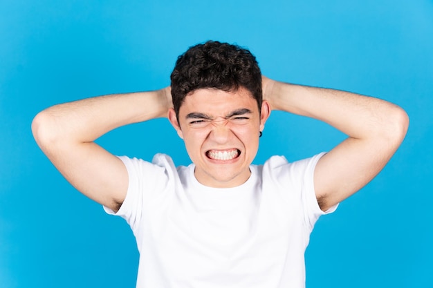 Foto wütend und verzweifelt hispanischer teenager junge hände auf kopf isoliert auf blauem hintergrund