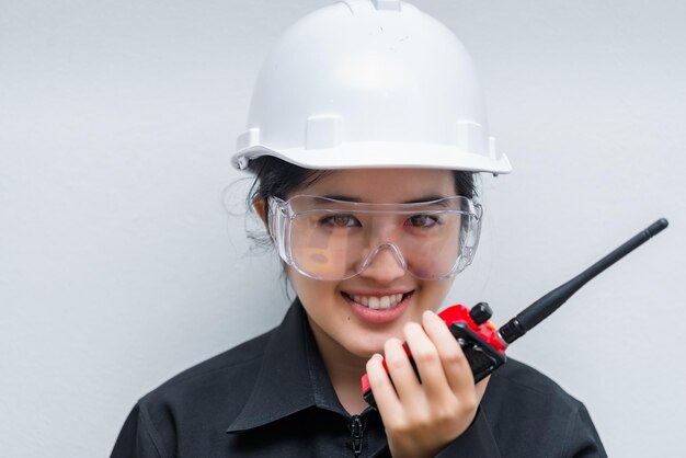 Wütende asiatische Ingenieurin, die eine Brille trägt und Funkkommunikation auf weißem Hintergrund verwendet. Thailand-Techniker verwenden Walkie-Talkie für die Arbeit