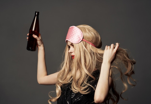 Wütende Frau mit einer Bierflasche in der Hand, mit hellem Make-up und einer rosa Schlafmaske, Foto in hoher Qualität