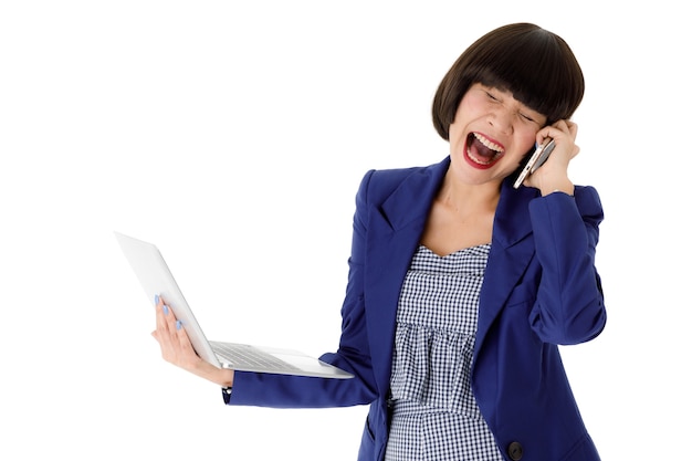 Wütende junge asiatische Büroangestellte im blauen Anzug, die offenen Laptop hält und ausdrucksvoll am Handy vor weißem Hintergrund schreit