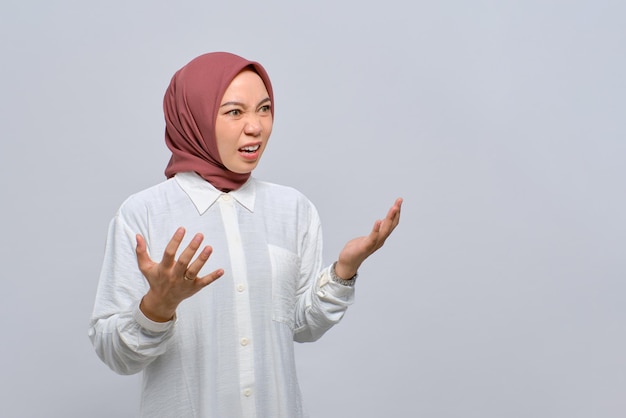 Wütende junge asiatische muslimische Frau, die Hände hebt und vor Wut schreit, isoliert auf weißem Hintergrund