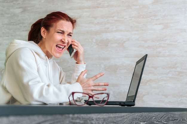 Wütende wütende freiberufliche frau, die an ihrem telefon schreit