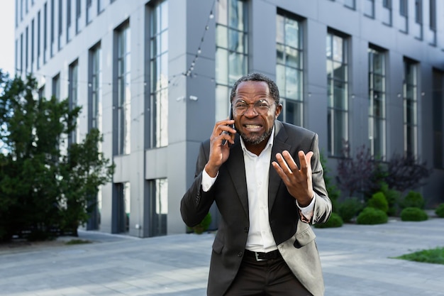 Wütender afrikanisch-amerikanischer Chef argumentiert und schreit, während er am Telefon telefoniert, ein älterer Mann im Geschäft