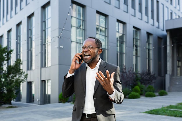 Wütender afrikanisch-amerikanischer Chef argumentiert und schreit, während er am Telefon telefoniert, ein älterer Mann im Geschäft