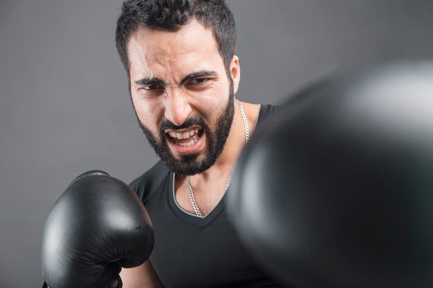 Wütender bärtiger Mann in Boxhandschuhen auf isoliertem grauem Hintergrund