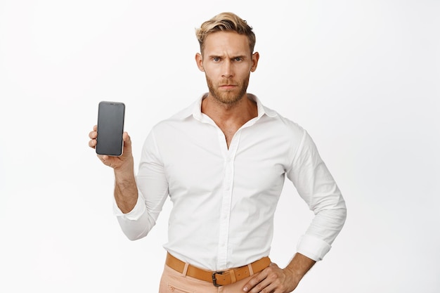 Wütender Geschäftsmann, der seinen Handybildschirm zeigt, runzelt die Stirn und enttäuscht den weißen Hintergrund