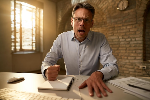 Wütender Geschäftsmann, der vor Frustration schreit, während er im Büro arbeitet und in die Kamera schaut