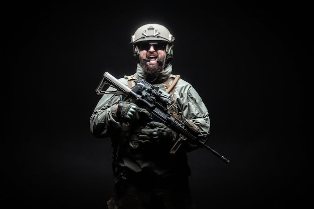 Wütender Soldat in Uniform mit einem Gewehr, das nachts im Stress auf schwarzem Hintergrund schreit