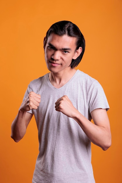 Wütender, starker junger asiatischer Mann, der in Kampfpose mit ernstem Gesichtsausdruck steht. Wütender Teenager in Boxposition mit geballtem Fäustenporträt, aggressiver Kämpfer, der in die Kamera schaut
