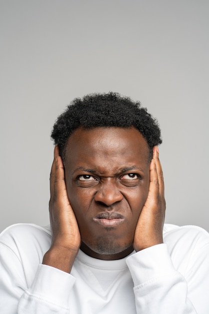 Wütender verrückter gestresster Afro-Mann, der seine Ohren bedeckt und aufschaut, hört störendes lautes Geräusch