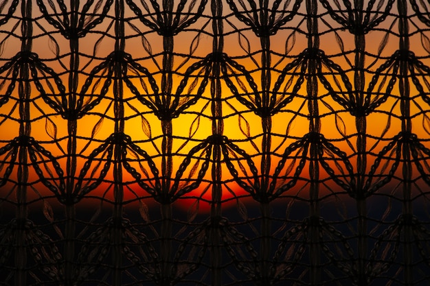 Wunderbar lebendige Morgendämmerung aus dem Fenster durch gemusterten Vorhang. Erstaunlicher warmer Himmel hinter Schattenbildern der Tüllbeschaffenheit. Orange Sonnenlicht. Strukturierter bunter Hintergrund der Gemütlichkeit mit Sonnenaufgang. Kopieren Sie Platz.