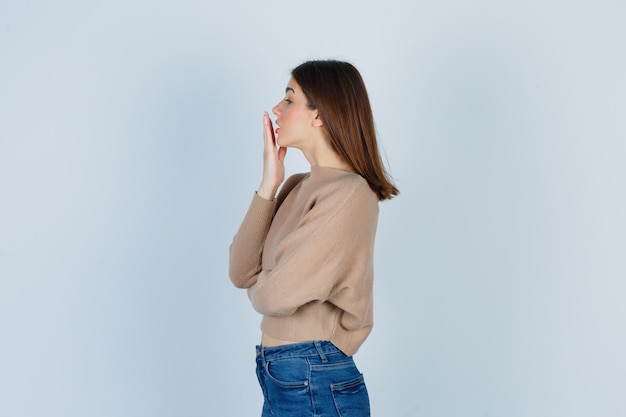 Wunderbare Dame mit Hand in der Nähe von Mund in Pullover, Jeans und schockiert.