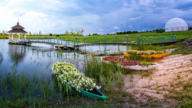 Wunderbare Sommerlandschaft und ein Ort für Meditationen. Ein Holzpavillon, eine Plattform und mehrere kleine Boote voller Blumen am See.