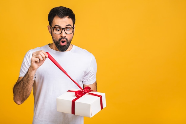 Wunderbares Geschenk! Entzückendes Foto des attraktiven bärtigen Mannes mit dem schönen Lächeln, das Geburtstagsgeschenkbox lokalisiert über gelbem Hintergrund hält.