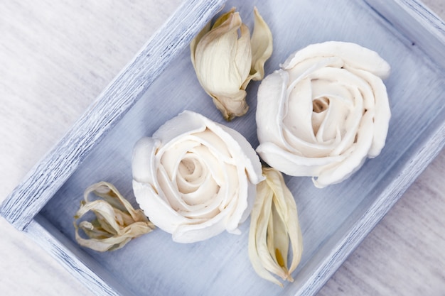 Wunderschön dekoriertes Dessert. Weiße Meringe in Form der Blumen auf hölzerner blauer Kiste auf Tabelle. Kalorienarme Süße. Apple Zephyr. Ansicht von oben.