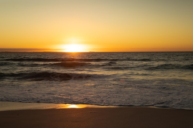 Wunderschöne Aussicht auf den Sonnenuntergang über den Meereswellen und den feinen Sand am Horizont.