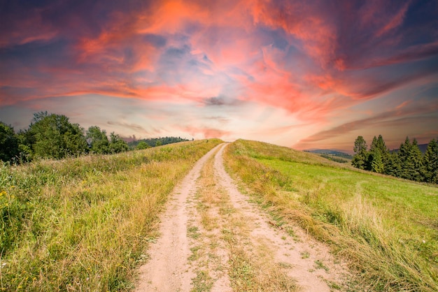 Wunderschöne Berge mit einer alten Straße, eingerahmt von einer orangefarbenen Sonne, die hell gegen den goldenen Himmel brennt