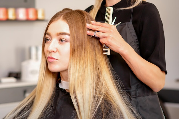 Wunderschöne blonde Frau mit langen Haaren und ihr Friseur, die Frisur suchen und überprüfen. Schöne Frisur einer jungen blonden Frau nach dem Sterben der Haare in einem Schönheitssalon, Ergebnisse der Haarbehandlung.