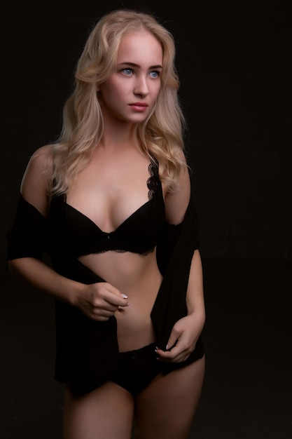 Wunderschöne Blondine in schwarzer Spitzenunterwäsche posiert auf schwarzem Hintergrund im Studio