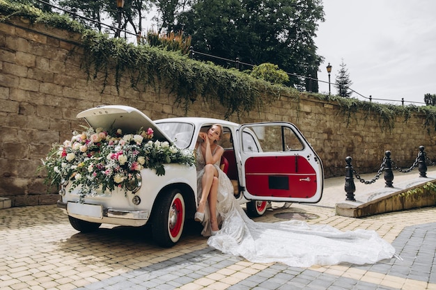 Wunderschöne Braut, die im Retro-Auto mit Blumen sitzt