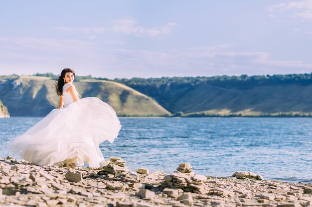 Wunderschöne Braut im weißen Luxuskleid, das an der Bucht lächelnd steht