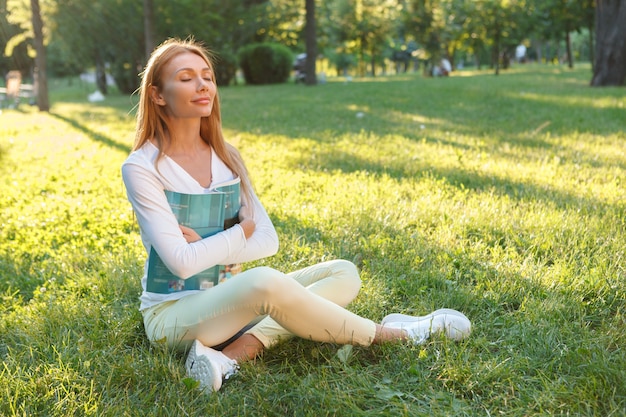 Wunderschöne Frau, die frische Luft atmet und auf dem Gras im Park sitzt