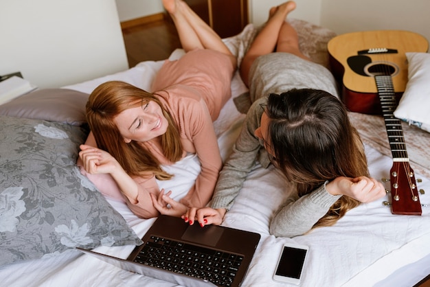 Wunderschöne Freunde, die den Laptop im Schlafzimmer benutzen. Bester Freund-Konzept.