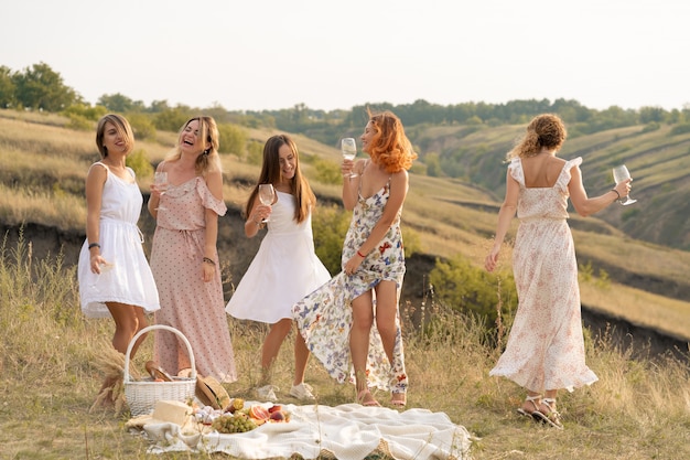 Wunderschöne Freundinnen, die Spaß haben und ein sommergrünes Picknick genießen, tanzen und Alkohol trinken. Personenkonzept.