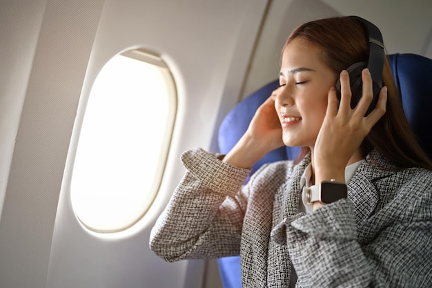 Wunderschöne Geschäftsfrau, die während des Fluges Musik über Kopfhörer hört Flugzeugtransport