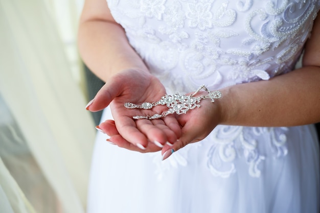 Wunderschöne Hochzeitsohrringe in den Händen der Braut an ihrem Hochzeitstag