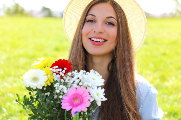 Wunderschöne junge Frau hält Blumenstrauß und schaut Kamera in einem Feld auf Frühling