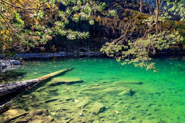 Wunderschöne Landschaft mit Bergsee und hohen Felsen mit beleuchteter Gipfelreflexion mit grünem Wasser, blauem, sauberem Himmel und gelbem Herbstsonnenaufgang