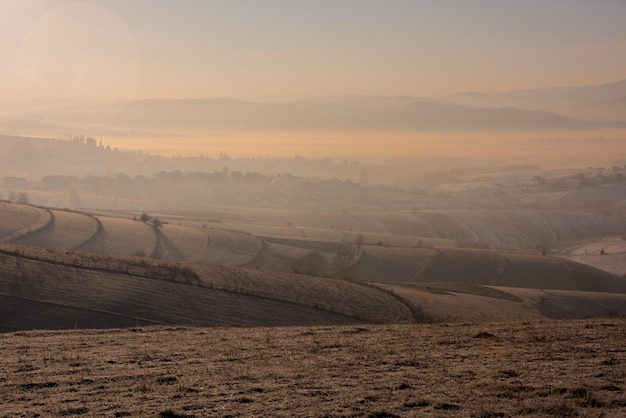 Wunderschöne Winterlandschaft bei Sonnenuntergang über schneebedecktem Feld mit Nebel und Verschmutzung im Tal dahinter