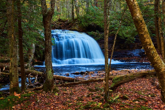 Wunderschöner großer blauer Wasserfall und Fluss mit Klippenwänden, abgefallenem Laub und Baumlichtungen