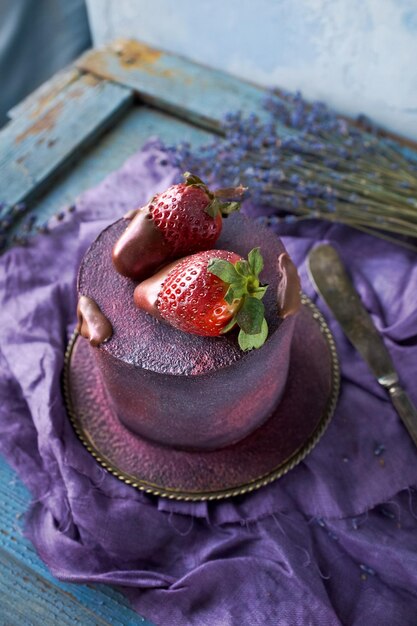 Wunderschöner lila Kuchen mit hausgemachten Kunstwerken, dekoriert mit Schokolade und Erdbeeren