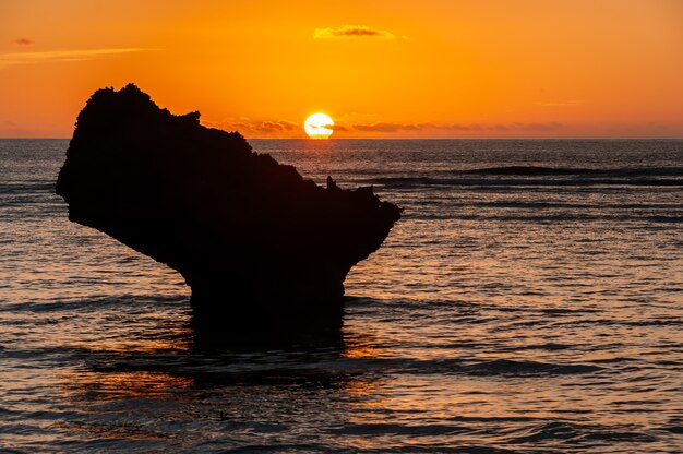 Wunderschöner orangefarbener Sonnenuntergang, der am Horizont hinter einem Küstenfelsen untergeht