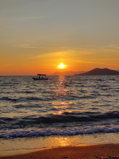 Wunderschöner Sonnenuntergang am Meer mit Wellen und Silhouette eines Bootes