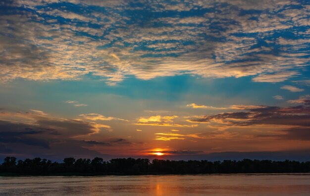 Foto wunderschöner sonnenuntergang mit wolken und die untergehende sonne unter dem horizont über dem wald und dem fluss