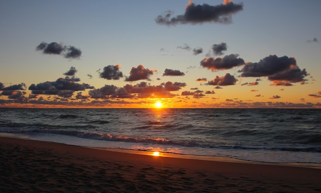 Wunderschöner Sonnenuntergang über dem Meer mit roten Reflexen auf Wolken und Meeresschaum-Sonnenscheibe am Horizont