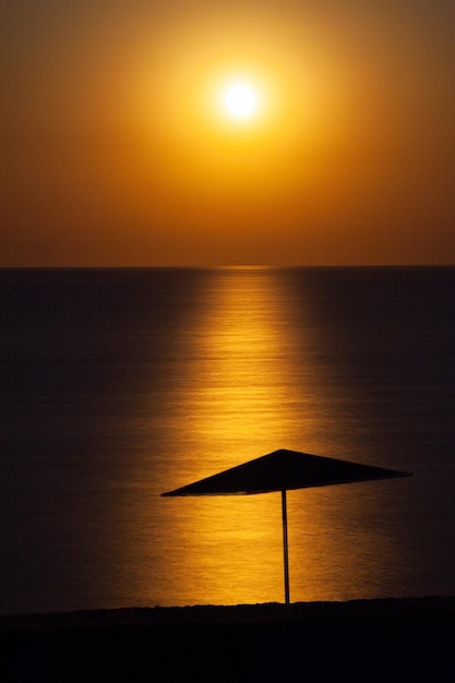 Wunderschöner und farbenfroher Sonnenuntergang vor dem Hintergrund der Silhouette eines Sonnenschirms am Meeresufer