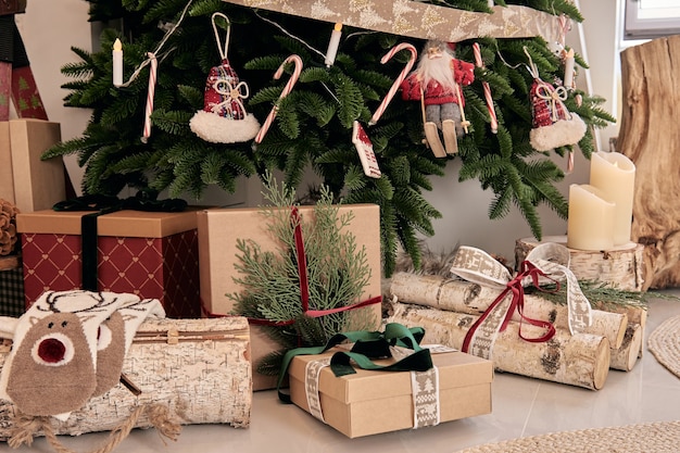 Wunderschöner Urlaub DIY handgemachte Heimtextilien. Gemütliches Zimmer mit Kerzen und Weihnachtsbaum mit Geschenken darunter. Heißgetränk auf dem Tisch. Neujahrsinterieur in einem Fotostudio