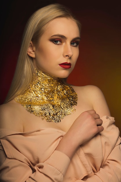 Wunderschönes blondes Model mit hellem Make-up und Goldfolie am Hals