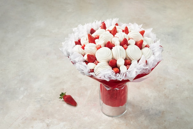 Wunderschönes Bouquet bestehend aus Marshmallows, reifen Erdbeeren und roten Süßigkeiten in einer Vase auf Marmor